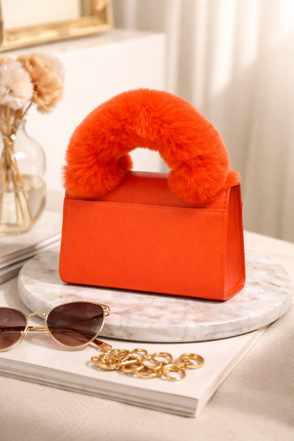 Orange handbag with fur handle on a marble surface with sunglasses and jewelry