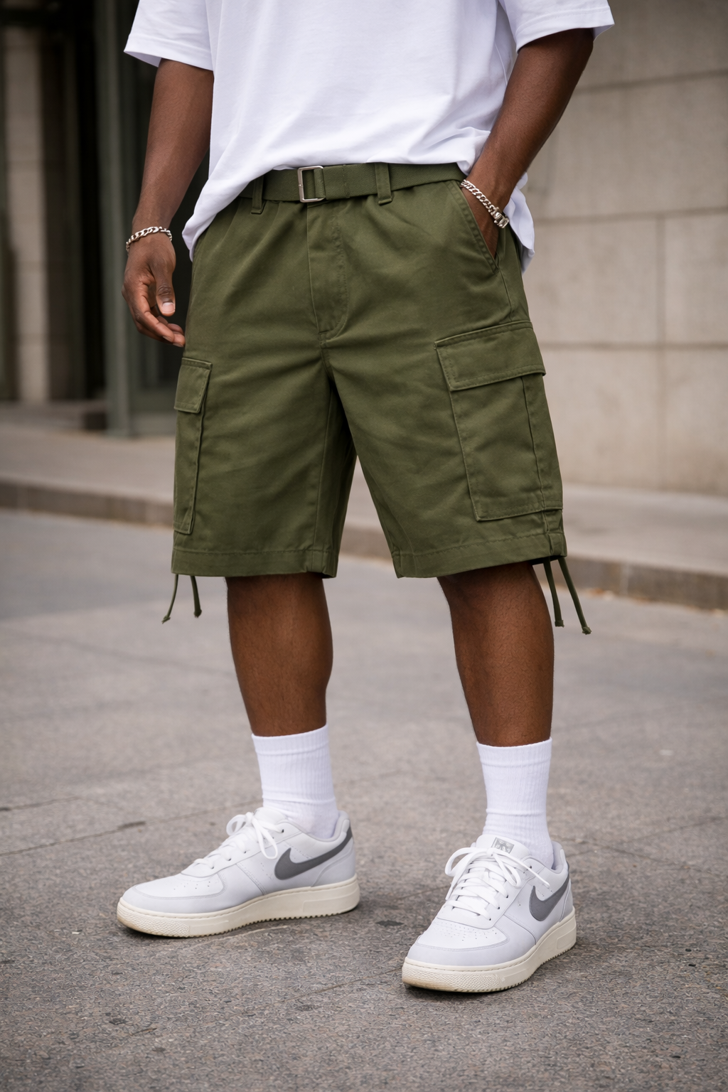 Person wearing green cargo shorts and white sneakers on a street.